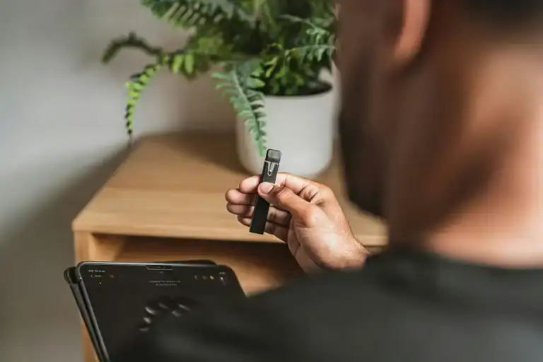 一名穿深色上衣的人手持外觀似電子煙的細長裝置，旁邊放著平板電腦。